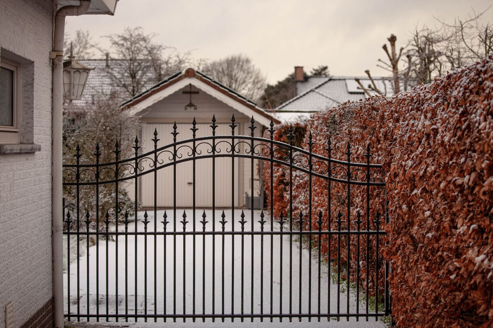 Black ornamental iron double gate with scrolled top rail across a snowy driveway