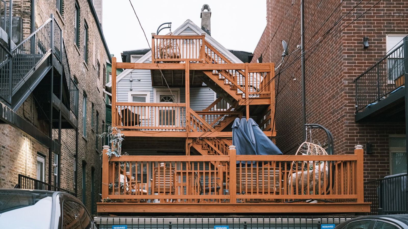 Stained wood multi-level deck with stacked landings and stairs behind a house between brick buildings